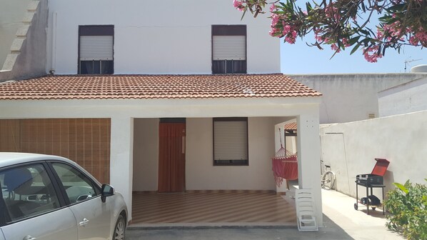 A two-story house with a tiled roof, a covered porch, and a car parked in the driveway. - Casa Vacanza Cala Spaghetti (Mazara del Vallo)