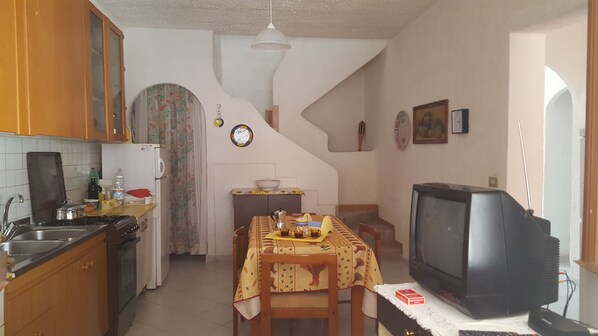 A kitchen with a stove, sink, and refrigerator. There is a dining table with chairs and a television. - Casa Vacanza Cala Spaghetti (Mazara del Vallo)