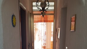 Un pasillo con suelo de baldosas, un candelabro y una puerta que da a un área exterior.