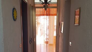 Um corredor com chão ladrilhado, um candelabro e uma porta que dá para área externa.