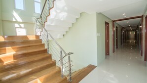 A modern interior with a wooden staircase, a glass railing, and a hallway leading to a door. - Shore Time Dormitel - Hostel (Boracay Island)