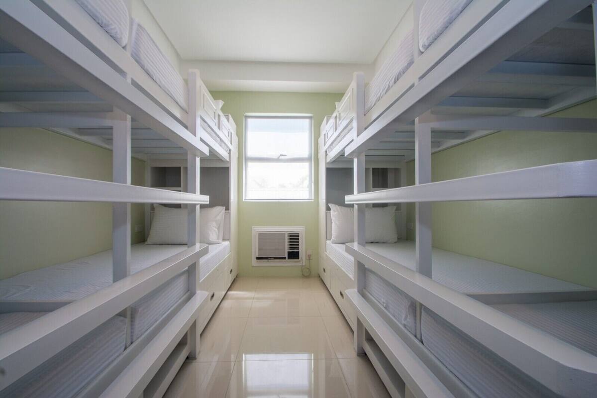 A narrow hallway with bunk beds on either side, a window at the end, and a radiator on the wall.