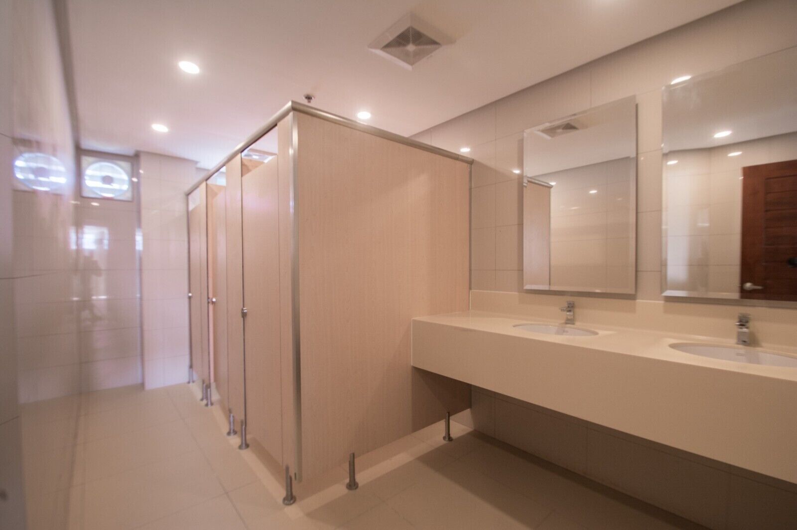 A modern bathroom with two sinks, a mirror, and a row of stalls.