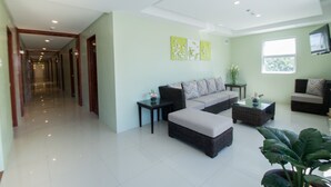 A spacious living area with a sofa set, a coffee table, and a television. There is a hallway leading to other rooms. - Shore Time Dormitel - Hostel (Boracay Island)