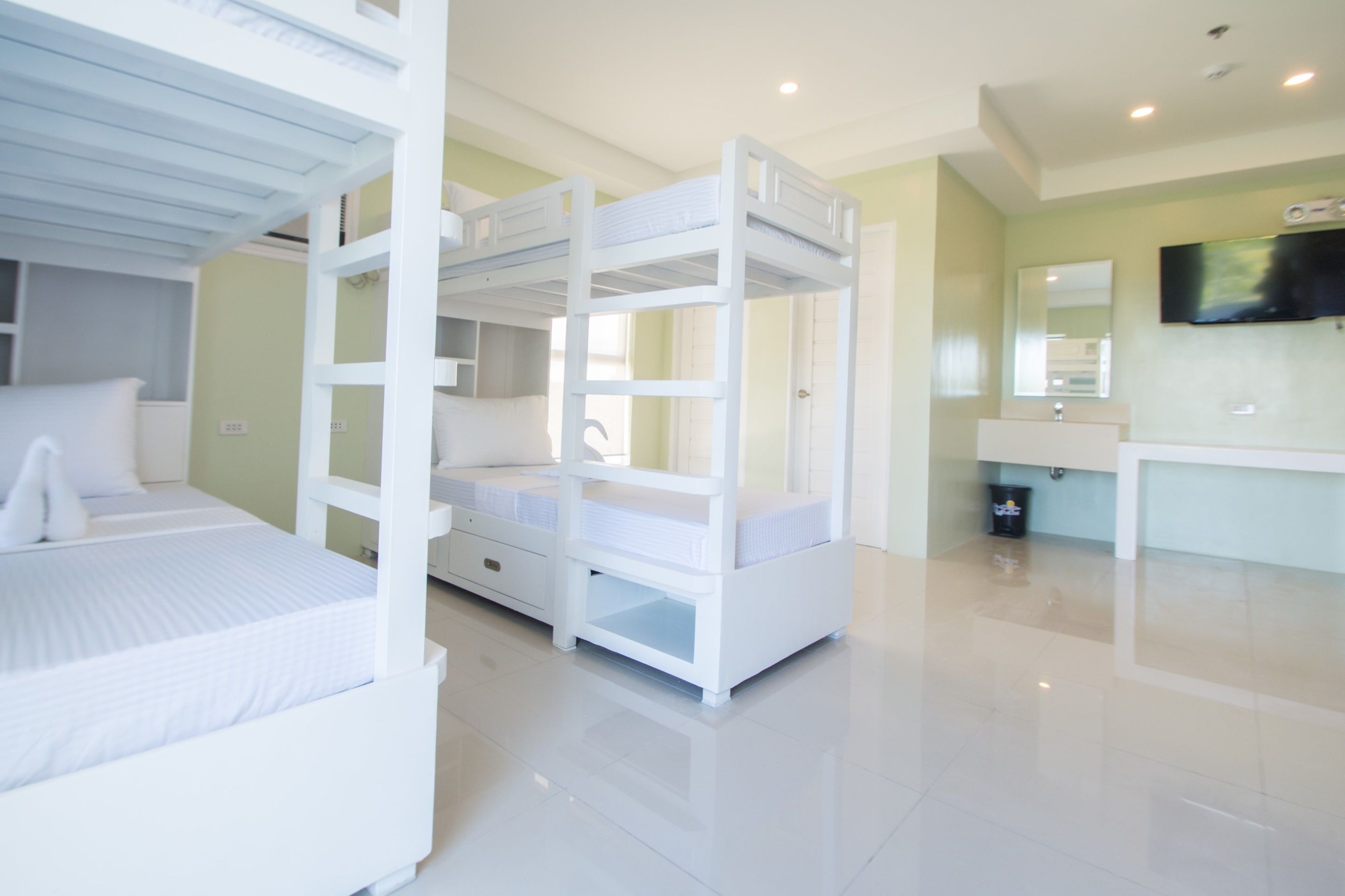 Un dormitorio con literas, un aparador, un tocador con espejo y un televisor en la pared.