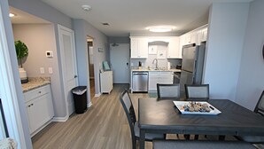 Une cuisine moderne avec des meubles blancs, des appareils en acier inoxydable et un coin repas avec une table dressée pour quatre personnes.