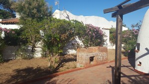 Une cour avec un four en briques, des murs blancs et des plantes en fleurs.