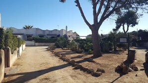 Un camino conduce a un edificio de fachada blanca y tejas de arcilla. Hay árboles y arbustos a lo largo del sendero, y un letrero que dice 