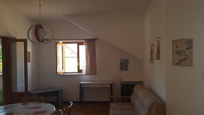 Une pièce comprenant une table à manger, un canapé, une fenêtre avec des rideaux, un petit bureau et des œuvres d’art accrochées au mur.