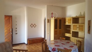 Un comedor con una mesa redonda cubierta con mantel, sillas de madera, un banco y un armario de madera con estantes.