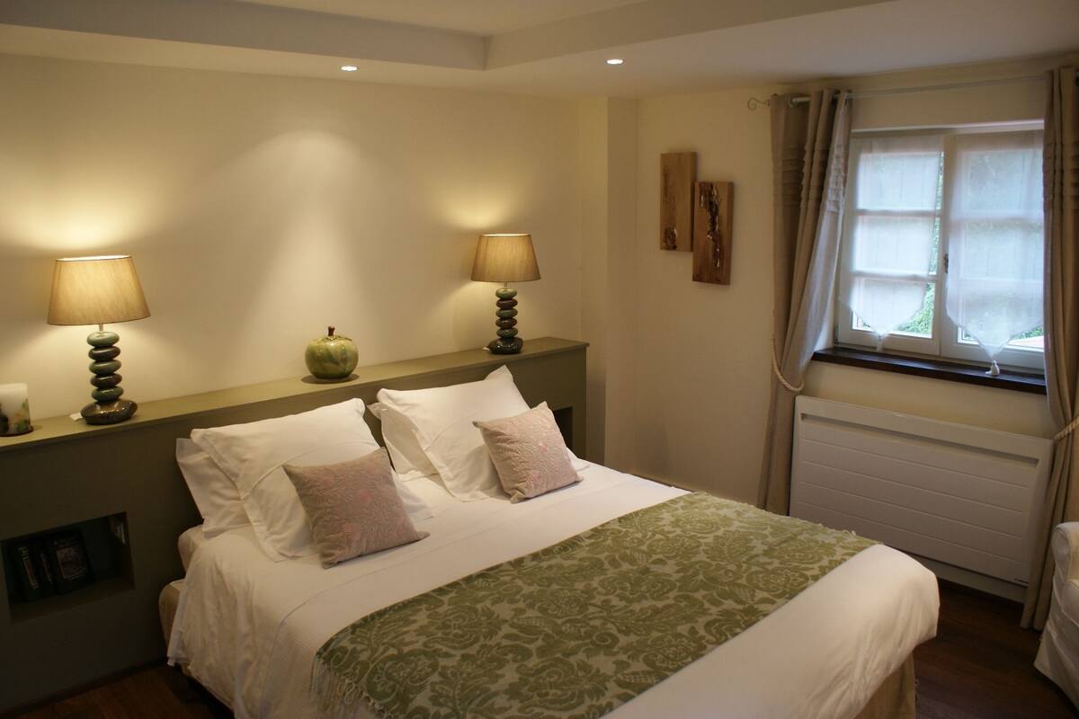 A neatly made bed with white and green linens, two bedside lamps, and a window with curtains.