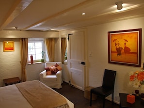A hotel room with a bed, a white armchair, a black chair, a small table with a vase of flowers, and a painting on the wall. - La Haute Grange (Fréland)