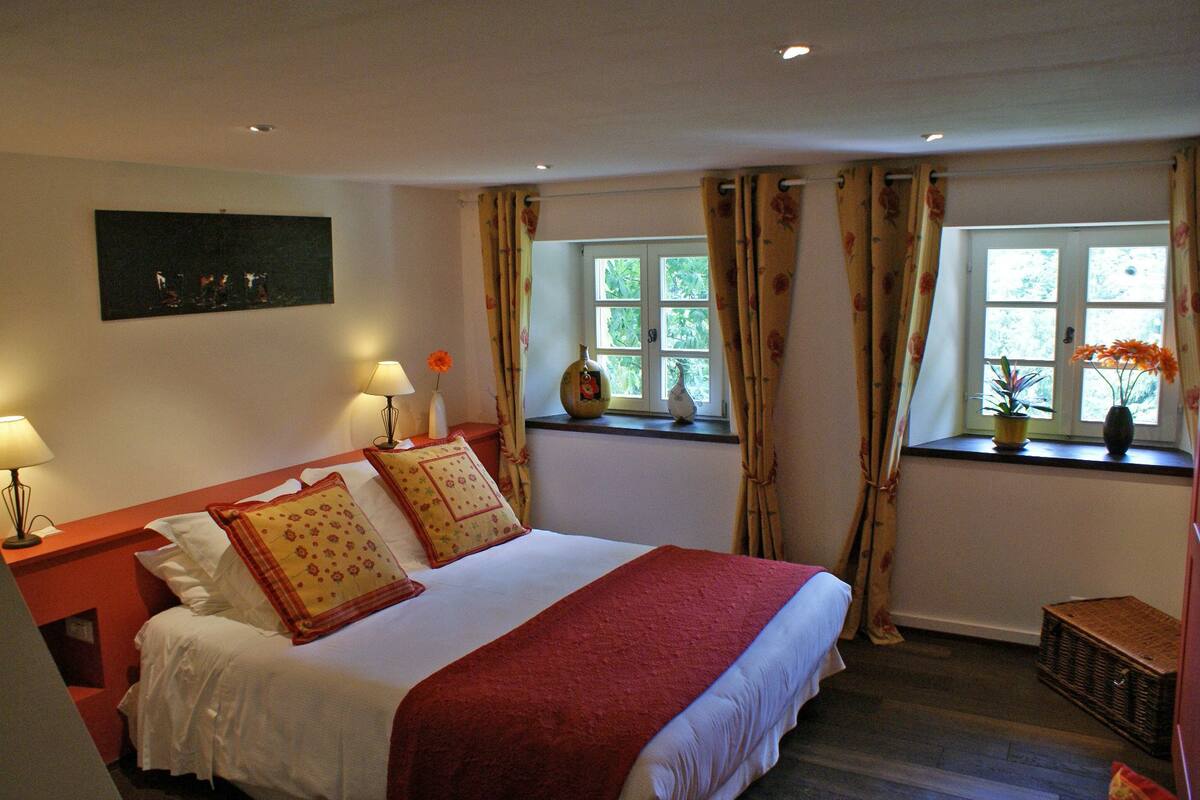 A hotel room with a large bed, two bedside lamps, a window with curtains, and a small table with a vase.