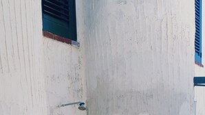 A corner of a building with white walls, a tiled floor, and a window with blue shutters.