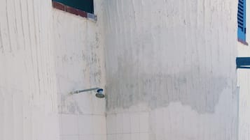 Canto de um edifício com paredes brancas, soalho em azulejos e uma janela com portadas azuis.