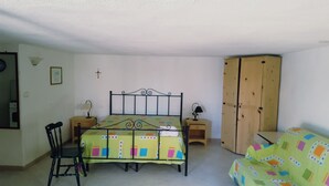 A bedroom with a bed, a chair, a wardrobe, and a small table with a lamp.