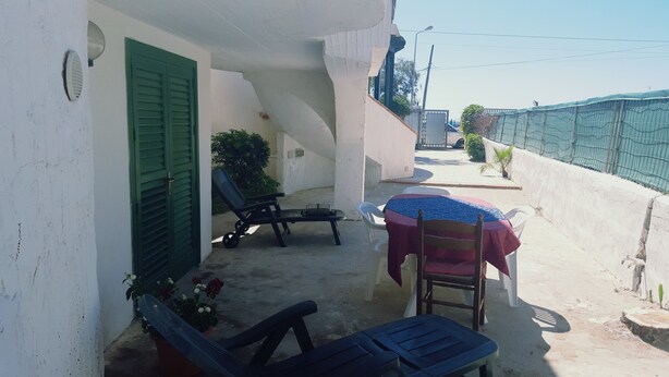 A balcony with a table covered by a tablecloth, two lounge chairs, and a potted plant.