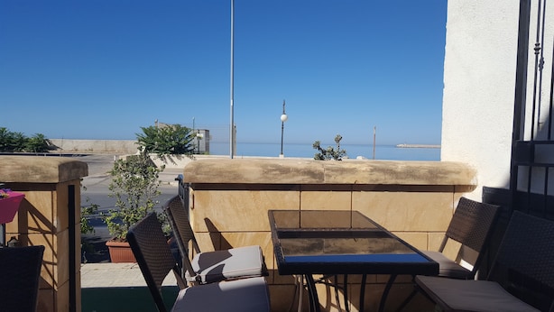 A terrace with a view of the sea, featuring a table and chairs, a potted plant, and a lamp post. - Viriglio Apartment (Mazara del Vallo)