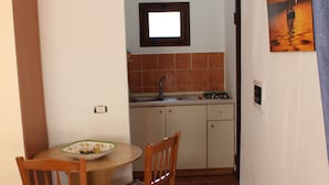 A compact kitchen with a dining area, featuring a tiled backsplash, a small sink, and a stove. - Viriglio Apartment (Mazara del Vallo)