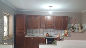 A kitchen with wooden cabinets, a sink, a stove, and a small decorative shelf with figurines. - Villa Valeria (Mazara del Vallo)