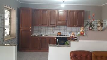 Uma cozinha com armários de madeira, pia, fogão e uma pequena estante decorativa com bonecas.