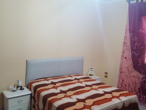 A bedroom with a bed, a nightstand, a decorative item, and a curtain.