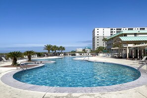 A large outdoor swimming pool with multiple lanes, surrounded by lounge chairs and palm trees.