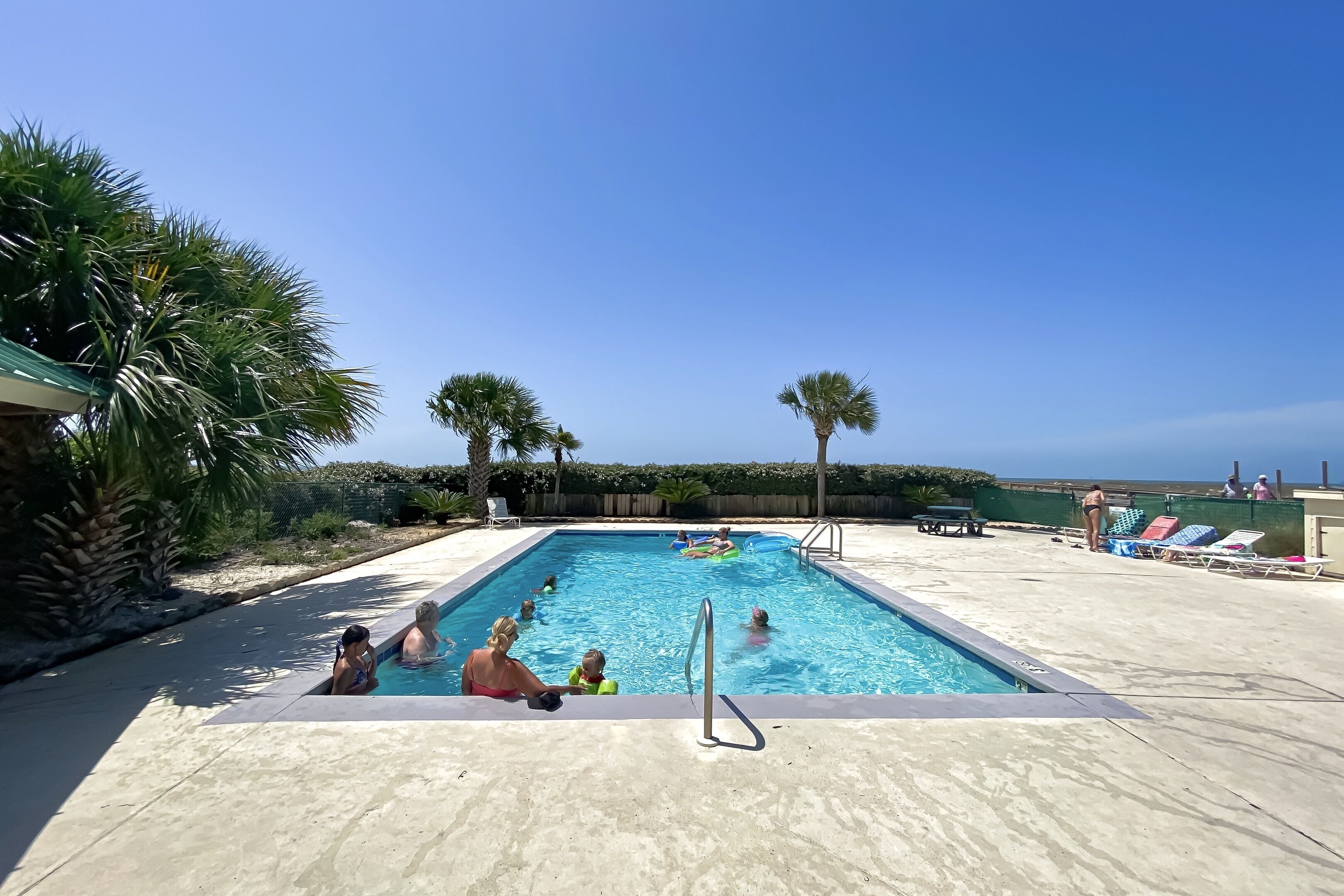 A swimming pool with a clear blue sky, palm trees, and lounge chairs.