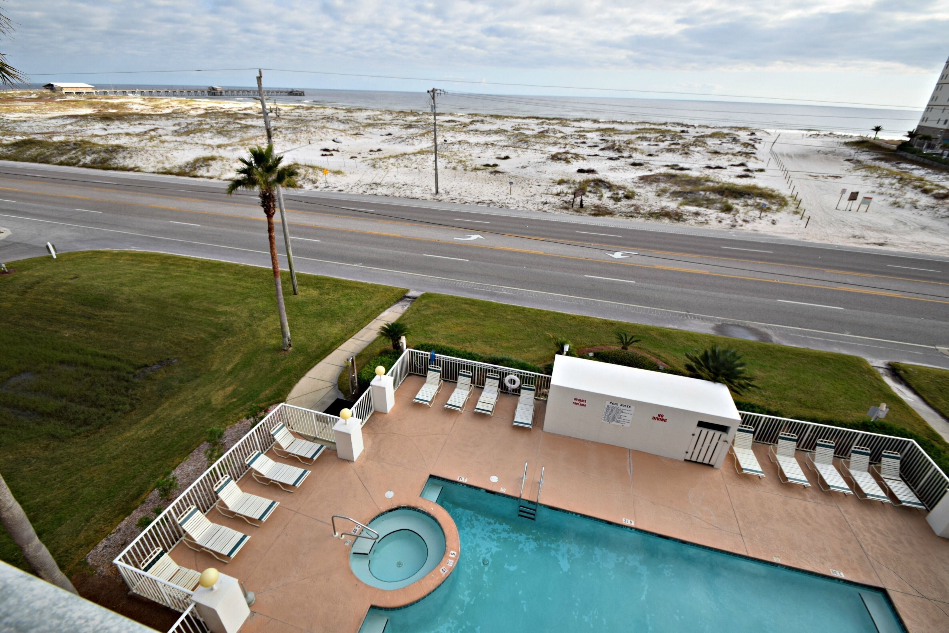 Un espace piscine doté de chaises longues, d’un jacuzzi et offrant une vue sur la plage et l’océan.