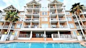 Un hotel a più piani con balconi, una piscina e palme.