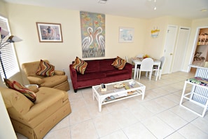 A living room with beige sofas, a red sofa, a white coffee table, and a dining area with a white table and chairs.