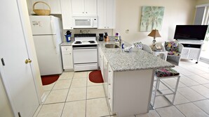 Una cucina compatta con mobili bianchi, un forno a microonde, un fornello e un lavello. C'è una piccola isola con una sedia, una televisione e un portatile.