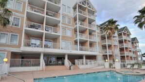 Un hotel a più piani con balconi, piscina e palme.