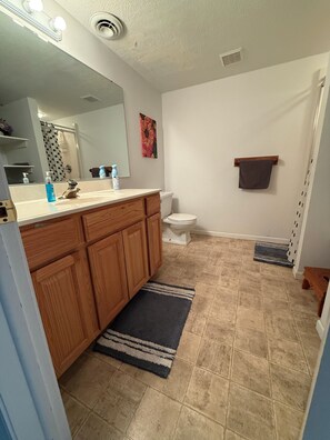 Ein Badezimmer mit Holzwaschtisch, Toilette, Duschvorhang, Handtuchhalter und einer kleinen Teppich.
