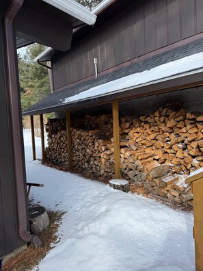 Ein überdachter Außenbereich mit einem Holzstapel und einem mit Schnee bedeckten Boden.
