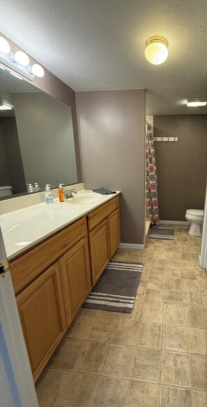 Une salle de bain avec un meuble-lavabo en bois, un grand miroir, un lavabo blanc et une douche avec un rideau à motifs.