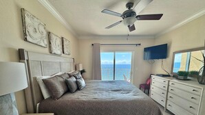 Un dormitorio con cama, mesita de noche, cómoda, ventilador de techo y televisor.