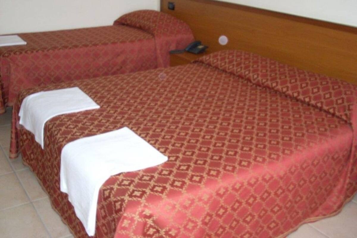 Ein Hotelzimmer mit zwei Einzelbetten, jeweils mit einem gemusterten Bettüberwurf und einer weißen Decke.