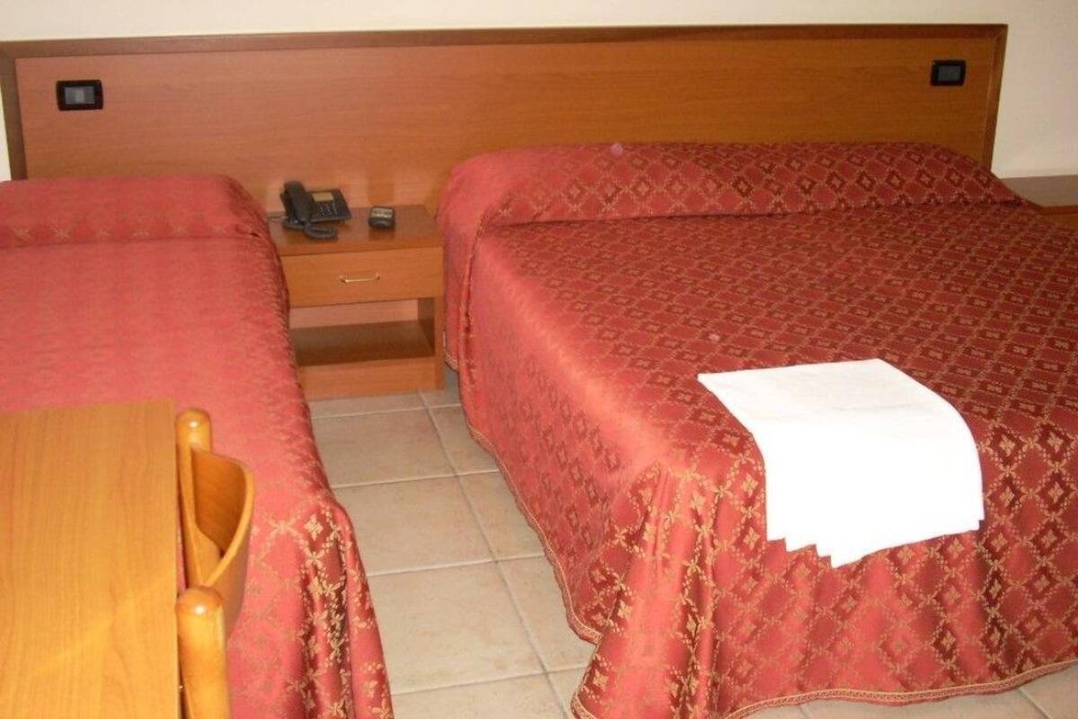 Ein Hotelzimmer mit zwei Betten, einem Holfnachtkästchen, einem Telefon und einem Sessel.