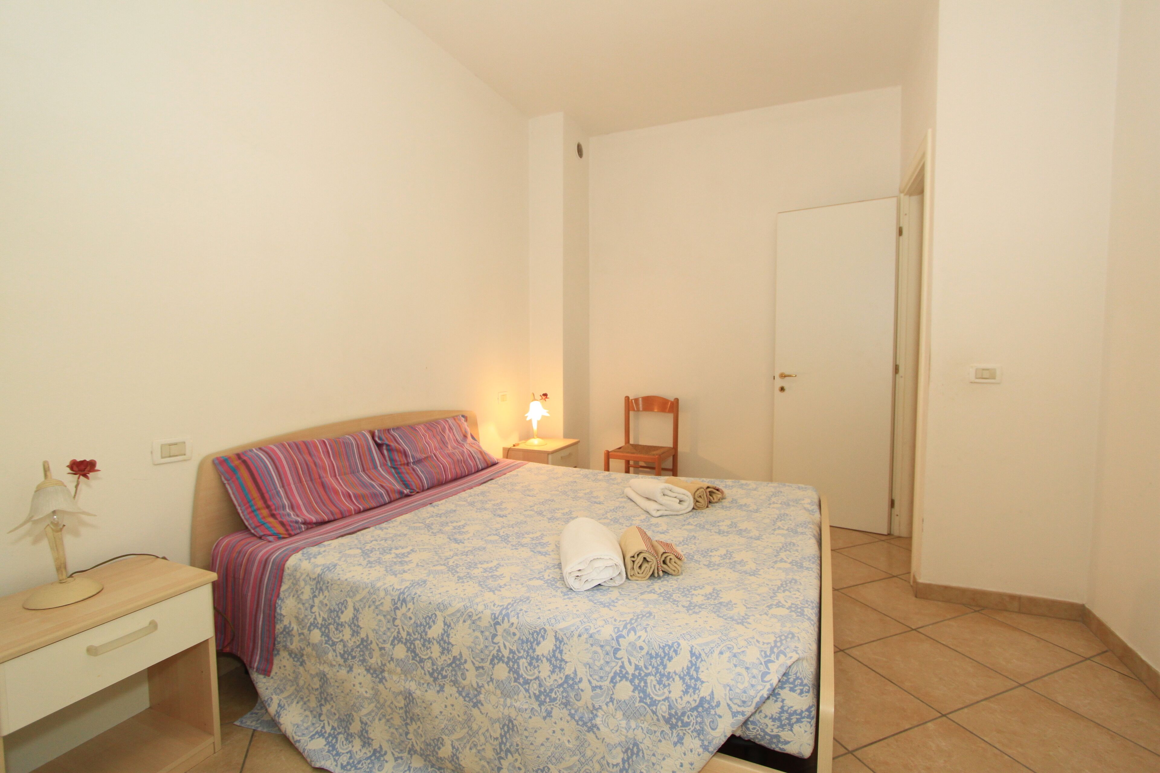 Une chambre à coucher avec un lit, une table de chevet, une chaise et une porte.