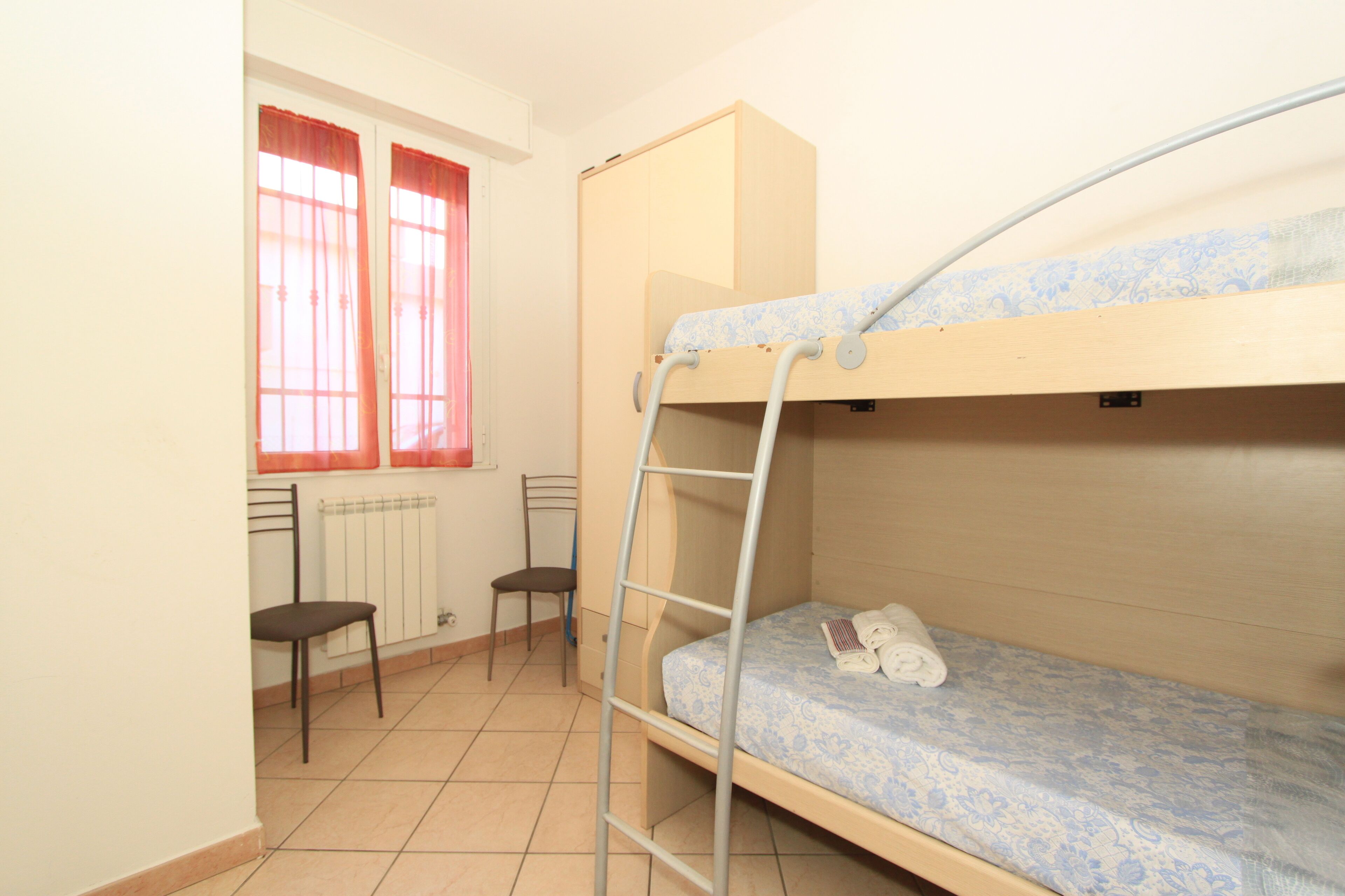A bunk bed room with a ladder, a desk, and two chairs.