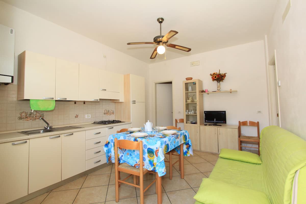 Cocina compacta con una mesa de comedor, sillas, ventilador de techo y sofá verde.