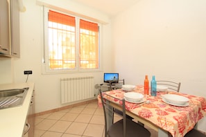 A small kitchen with a window, a dining table set with plates and cutlery, and a computer on a desk. - San Remo Apartments (Comacchio)