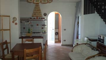 Uma cozinha com painel de azulejos, mesa de jantar com cadeiras, sofá e área de lavanderia visível por uma porta aberta.