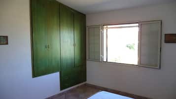 Quarto com uma cama, um guarda-roupa grande verde e uma janela com persianas.