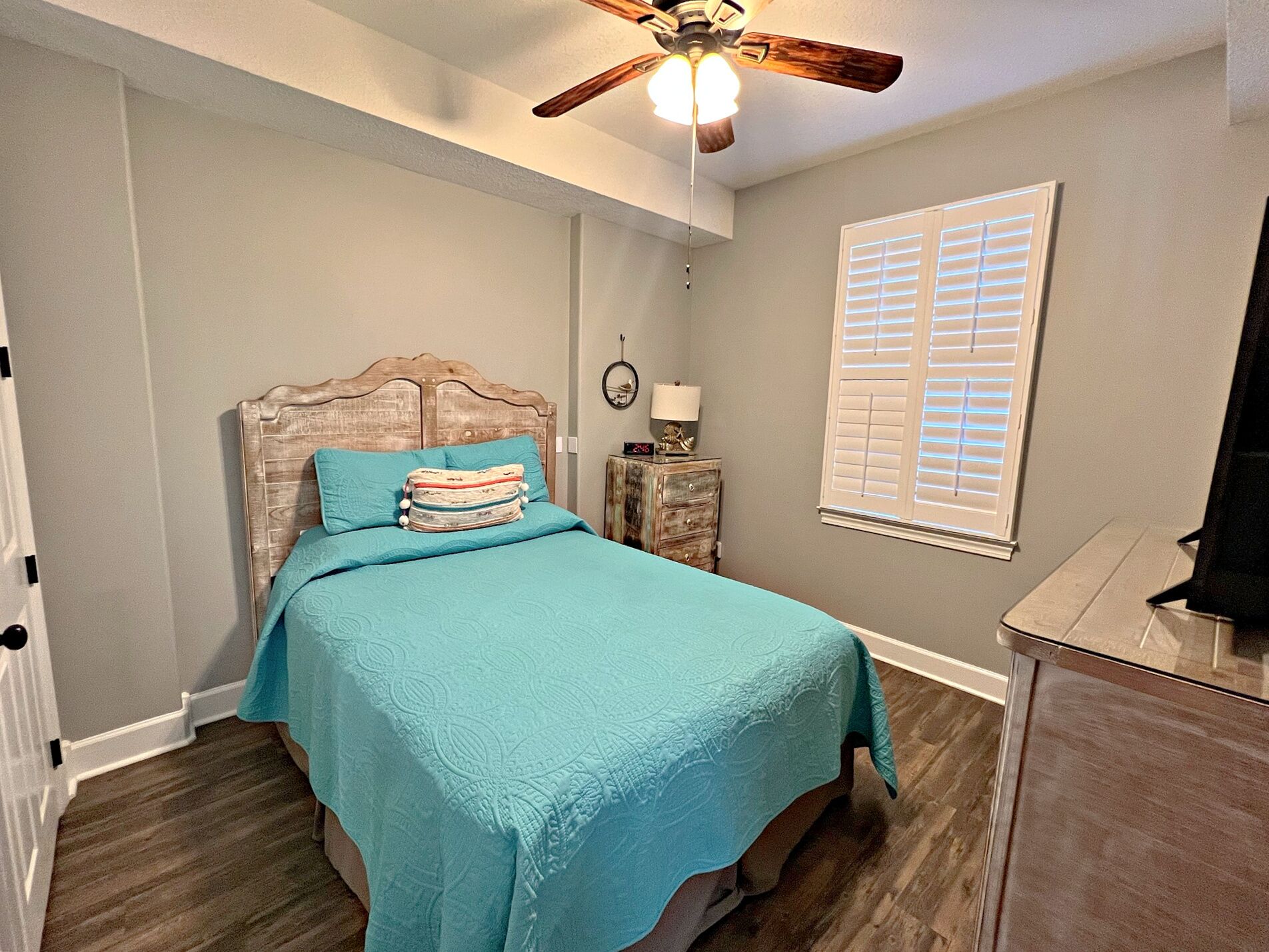 A bedroom with a bed, a ceiling fan, a nightstand, a lamp, and a window with blinds.
