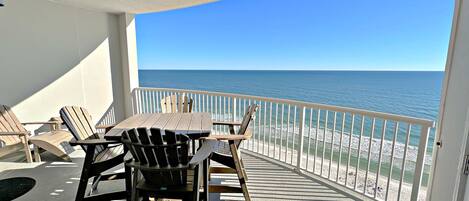 Een balkon met uitzicht op de oceaan, voorzien van houten stoelen en een tafel.