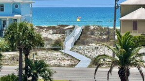 Eine Küstenstraße führt zu einem Strand mit einer Flagge, Palmen und Häusern.