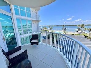 A balcony with a view of a beach and a pool, furnished with wicker chairs and a table. - Relax and Catch a couple of fish! 🎣 ~ There is something for everyone! (Gulf Shores)
