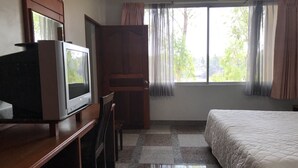 Habitación de hotel con cama, televisor sobre un mueble de madera, escritorio con silla y ventana con cortinas.